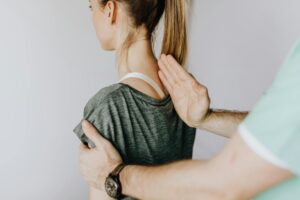 crop anonymous chiropractor examining spine of fit lady in hospital